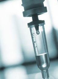 Close-up of an IV infusion drip chamber with a single droplet falling, clinical blue tones suggesting a hospital or clinic setting