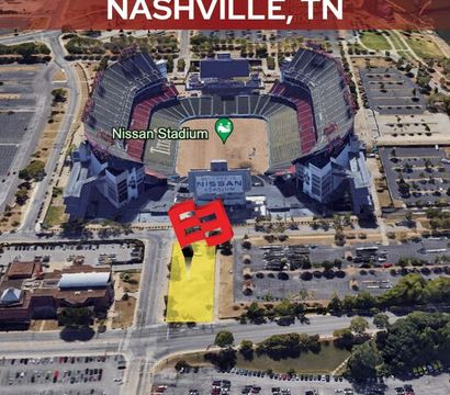 Aerial view of a large football stadium at 100 Woodland Street, Nashville, TN, with a yellow-highlighted vacant lot and red location marker in front, surrounded by parking lots and city streets.