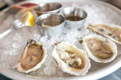 Fresh raw oysters on the half shell on crushed ice in a metal tray, served with a lemon wedge and metal cups of cocktail sauce and mignonette — chilled seafood platter.