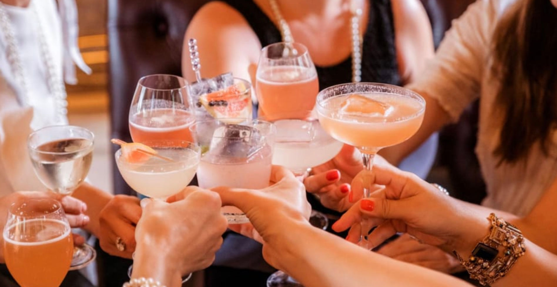 Friends clinking colorful cocktails in stemmed glasses for a celebratory toast at a lively bar