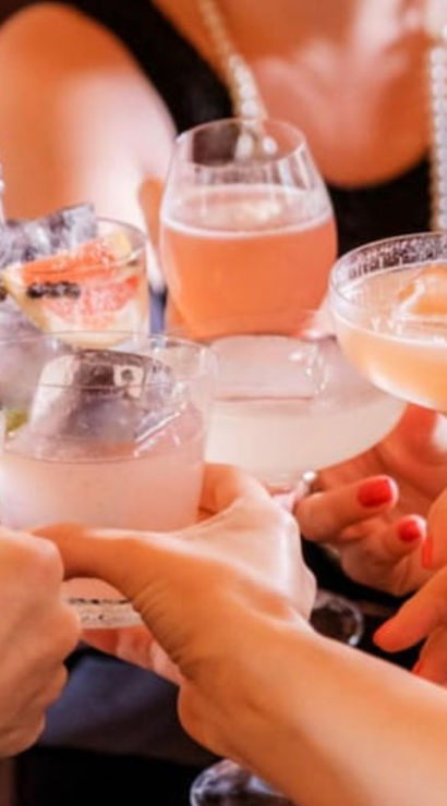 Friends clinking colorful cocktails in stemmed glasses for a celebratory toast at a lively bar