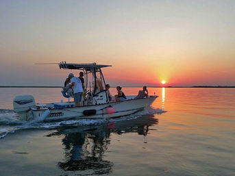 Motorboat with a small group on a sunset cruise across calm coastal waters, orange-pink sky and sun reflecting on the surface.