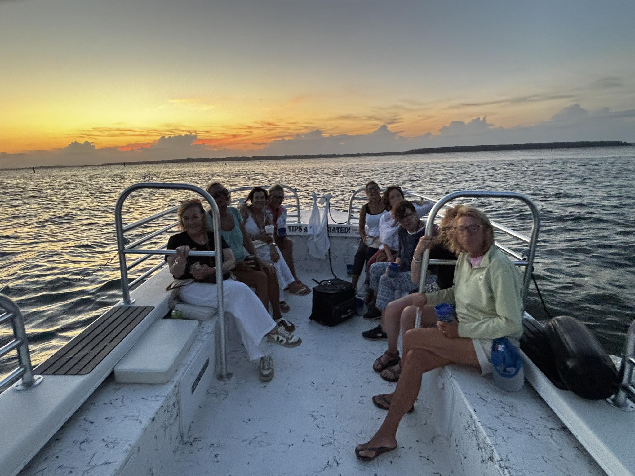 Group of passengers on a small boat enjoying a coastal sunset cruise, calm ocean waters and a colorful sky on the horizon.