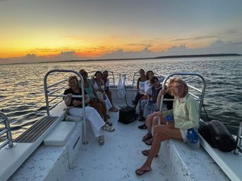 Group of passengers on a small boat enjoying a coastal sunset cruise, calm ocean waters and a colorful sky on the horizon.