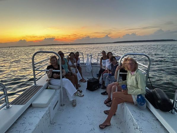 Group of passengers on a small boat enjoying a coastal sunset cruise, calm ocean waters and a colorful sky on the horizon.