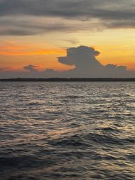 Orange and yellow sunset over open ocean with rippling water and a towering dark cloud formation on the horizon