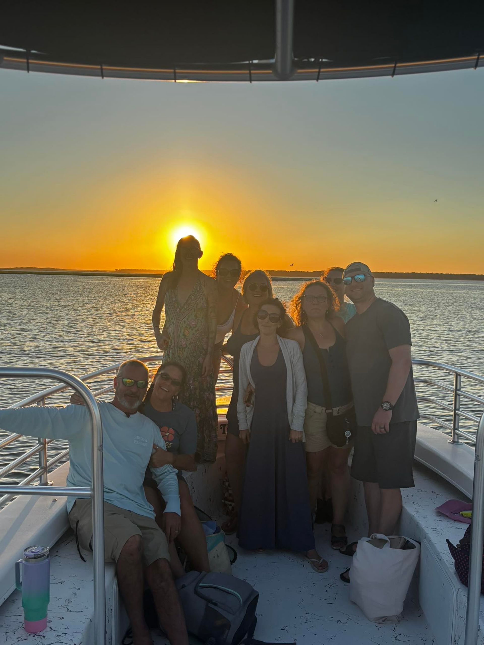 Group of people on a boat deck at golden sunset over a calm coastal bay, relaxed summer outing