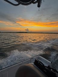 Golden sunset over coastal waters seen from a boat, orange clouds reflecting on rippling waves and a foamy wake in the foreground.