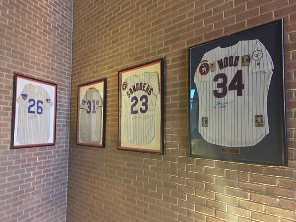Sports-memorabilia corner with four framed pinstripe baseball jerseys numbered 26, 31, 23 and 34 mounted on a red brick interior wall.