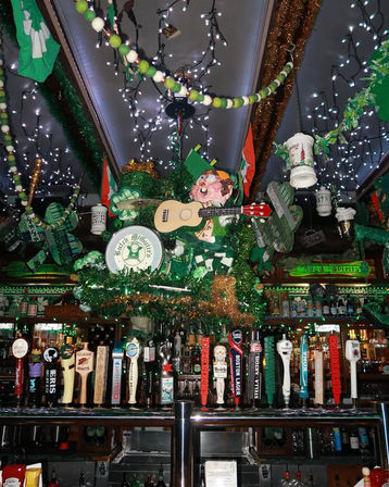 Vibrant Irish-pub interior decked in green tinsel, shamrocks and string lights, a whimsical leprechaun figure holding a small guitar suspended above a colorful row of beer tap handles.