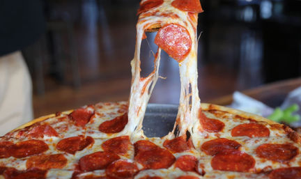 Hot pepperoni pizza slice pulled up with long, stretchy melted mozzarella from a golden-crusted pizza in a casual pizzeria setting