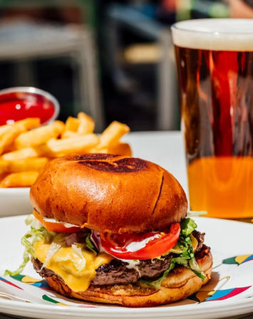 Juicy cheeseburger with melted cheddar, lettuce and tomato on a toasted bun, served with golden fries, ketchup and a pint of amber beer on a diner plate