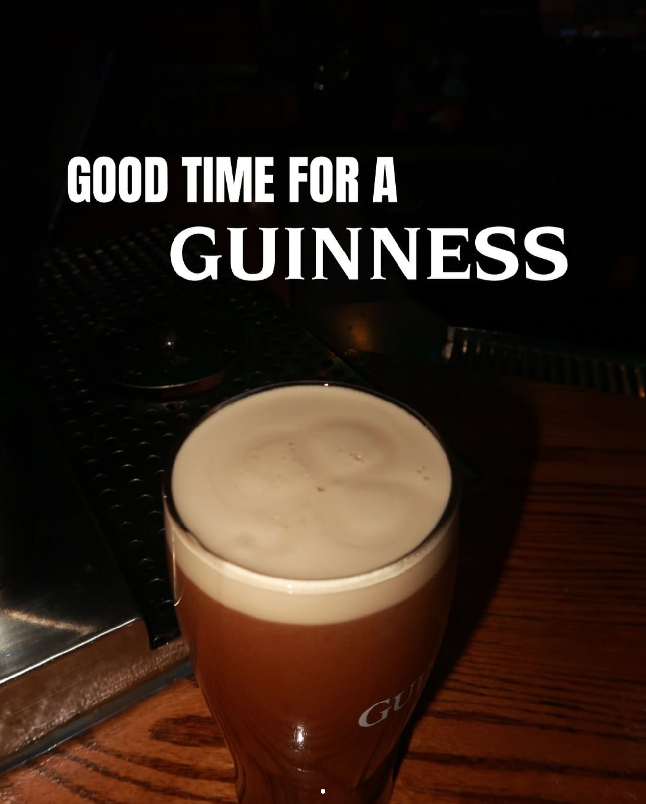 Creamy stout pint with a thick tan head on a wooden bar counter in a dimly lit pub beneath bold promotional 'Good time' text.