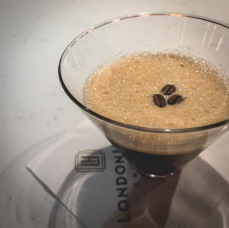 Frothy espresso martini in a martini glass topped with three coffee beans, resting on a white napkin on a marble countertop.