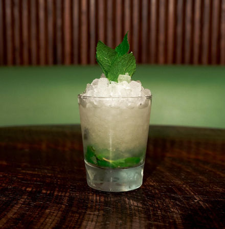 Chilled mint cocktail in a short glass piled with crushed ice and fresh mint leaves on a rustic wooden table with a green backdrop