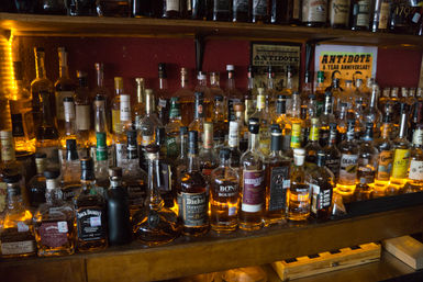 Backlit display of bourbon and whiskey bottles on a wooden bar shelf glowing warm amber in a cozy pub