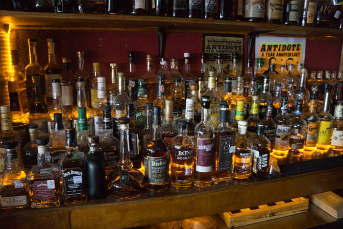 Backlit display of bourbon and whiskey bottles on a wooden bar shelf glowing warm amber in a cozy pub