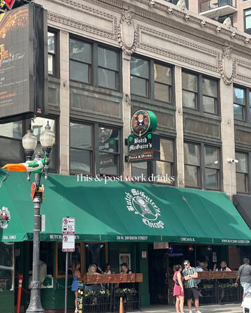 Downtown Chicago Irish-style pub with a large green awning and sidewalk patio, patrons chatting under an ornate stone façade and a lamppost draped with an Irish flag.