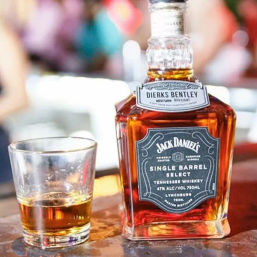 Close-up of a Jack Daniel's Single Barrel Select Tennessee whiskey bottle next to a partially filled shot glass on a bar counter, warm amber liquid and blurred background.