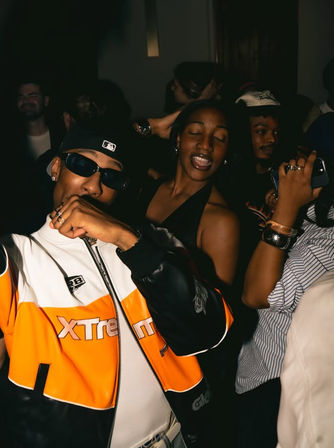 Crowded urban nightclub scene with a man in an orange jacket and sunglasses posing while a woman dances with her eyes closed, lively city nightlife vibe.