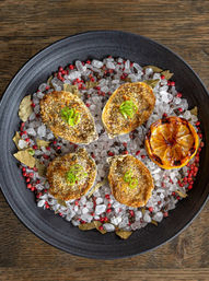 Gourmet baked oysters on the half shell with golden breadcrumb crust and sliced scallion, plated on crushed sea salt and pink peppercorns with bay leaves and a charred lemon half on a black plate — coastal seafood appetizer.