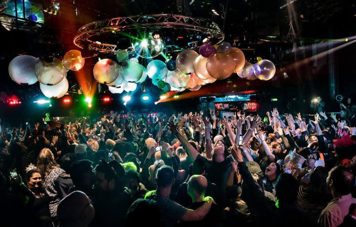 Packed nightclub dance floor with cheering crowd under disco balls and colorful stage lights