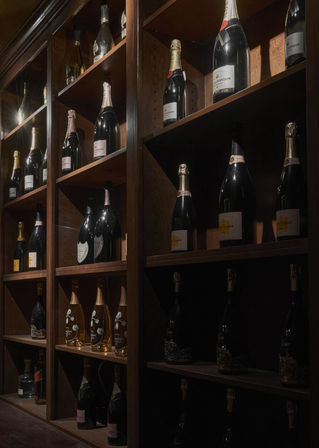 Dimly lit wine cellar with dark wood shelving showcasing assorted champagne and sparkling wine bottles glinting on cubby shelves