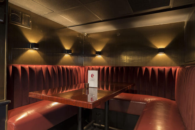 Dimly lit cozy lounge booth with deep red velvet banquette seating, glossy wooden table, and warm wall sconces casting ambient light