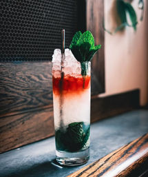 Refreshing mint cocktail with crushed ice, red liqueur float and mint sprig in a tall glass on a wooden bar counter