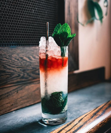 Refreshing mint cocktail with crushed ice, red liqueur float and mint sprig in a tall glass on a wooden bar counter