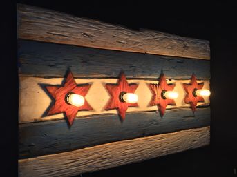 Rustic wooden wall light panel with weathered blue and white planks and five red star-shaped mounts, each fitted with a glowing vintage Edison bulb for warm ambient lighting.