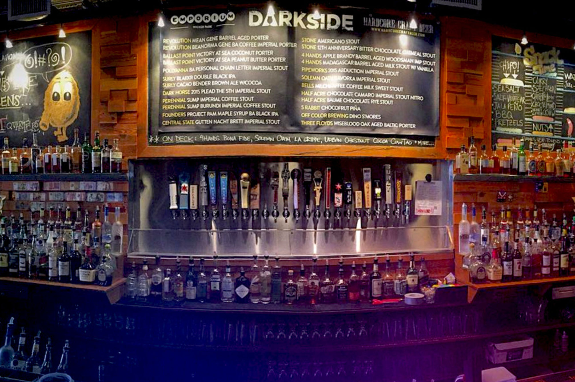 Wood‑paneled craft beer bar interior with a long row of beer taps beneath a large chalkboard beer list, flanked by shelves of liquor bottles and warm ambient lighting.