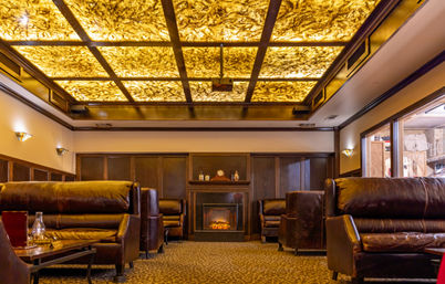 Warm, cozy lounge with dark leather sofas, patterned carpet, glowing fireplace and an amber backlit coffered ceiling