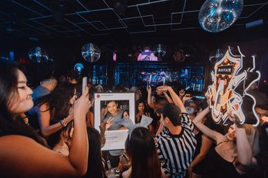 Crowded urban nightclub dance floor with people taking selfies in a giant social-media frame, disco balls, neon crest sign and blue party lighting