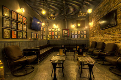 Cozy industrial-style lounge interior with leather sofas and swivel chairs, exposed brick wall, framed vintage posters, low metal tables and warm Edison-bulb lighting.