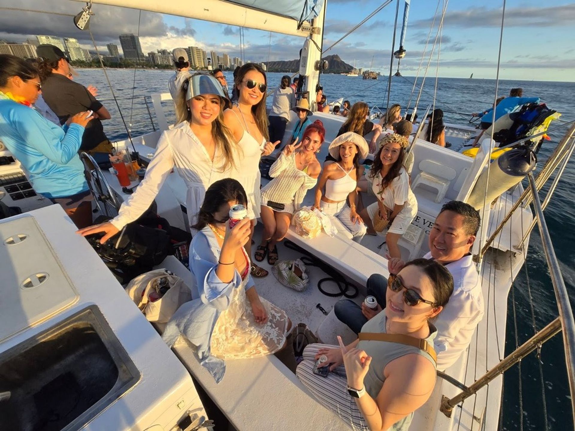 Smiling group of people enjoying a sunset catamaran cruise off Waikiki, Oahu, with the Honolulu skyline and Diamond Head crater on the horizon.