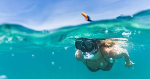 Snorkeler wearing mask and snorkel gliding through crystal-clear turquoise tropical ocean in a split-surface shot with bubbles rising