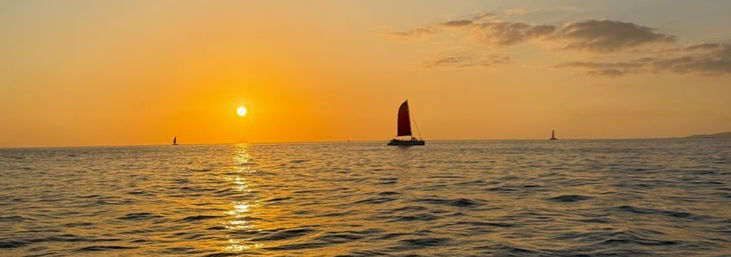 Golden ocean sunset – red‑sailed boat glides across calm water with the sun’s shimmering reflection on the horizon.