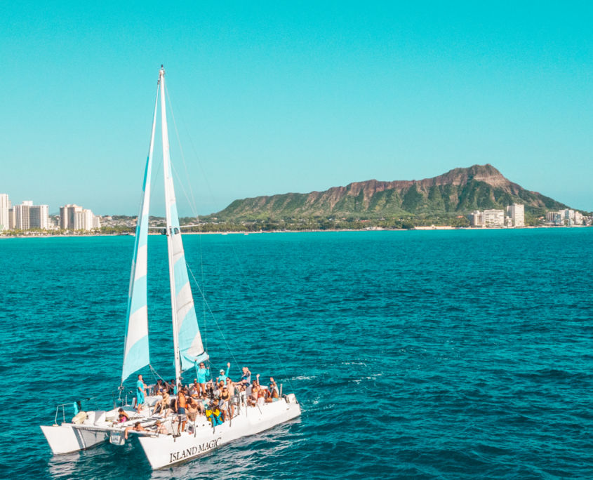 Crowded white catamaran tour sailing on turquoise Pacific near Waikiki with Diamond Head crater and Honolulu skyline in the background