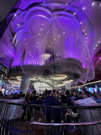 Upscale Las Vegas casino lounge with dramatic cascading crystal‑string chandelier glowing purple above a busy central bar and seated patrons.