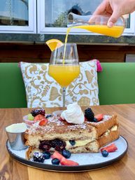 Brunch scene: stuffed French toast with custard and fresh berries, whipped cream and butter, plus a mimosa being poured on a sunny patio