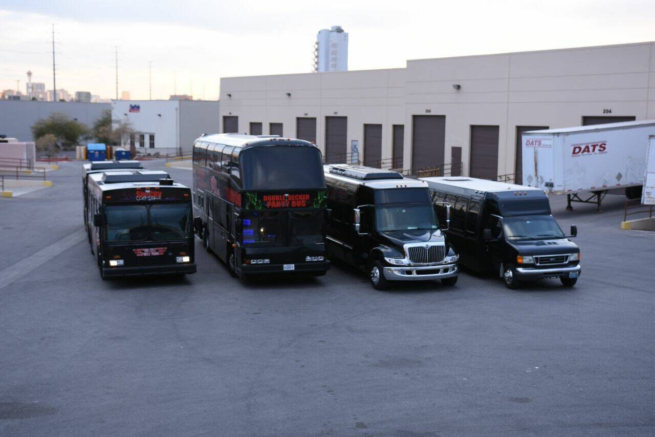 Black fleet of party and shuttle buses, including a double-decker, lined up in a warehouse loading lot at dusk.