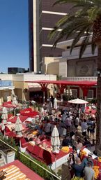 Vibrant Las Vegas hotel pool party with red daybeds and cabanas, palm trees, umbrellas and crowds lounging and mingling under a bright blue sky