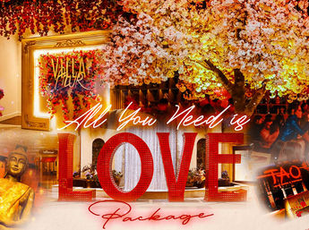 Vibrant romantic luxury resort event scene featuring giant red “LOVE” letters and “All You Need is” script in front of a fountain, glowing cherry blossom tree, floral wall, golden Buddha statue and warmly lit dining guests