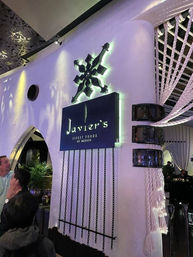Upscale Mexican restaurant interior with glowing logo on a curved white wall, dangling chains and thick braided ropes, purple mood lighting and diners in the foreground.