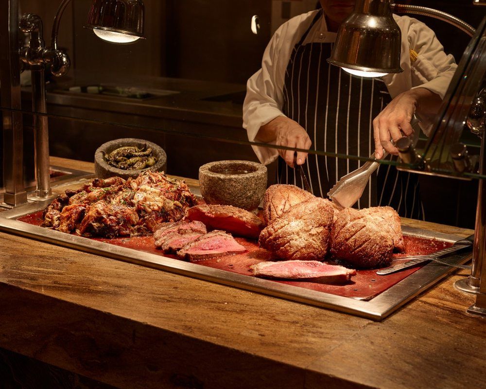Restaurant carving station with a chef slicing juicy medium‑rare roast beef and golden‑crusted roasts under warming lamps