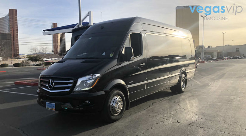 Sleek black Mercedes shuttle van parked in a sunlit Las Vegas parking lot with hotel towers and cracked asphalt in the foreground.