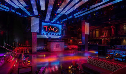 Upscale urban nightclub interior with polished dance floor, raised DJ booth and large LED screen, vibrant blue and magenta lighting, plush VIP booths and candlelit lounge tables