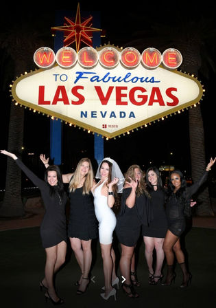 Six women, a bride in white with veil and friends in black, posing at night beneath the illuminated Welcome to Fabulous Las Vegas Nevada sign