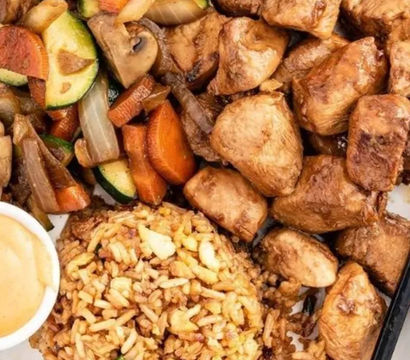 Savory teriyaki chicken bowl with cubed glazed chicken, zucchini-carrot-mushroom stir-fry, seasoned fried rice, dipping sauce and chopsticks
